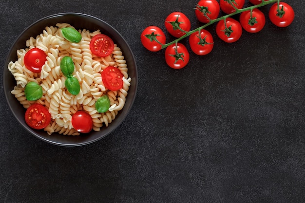 Fusilli kochte Teigwaren mit Tomatenkirsche und Basilikum auf Draufsichtraum des dunklen Hintergrundes, um Text zu kopieren