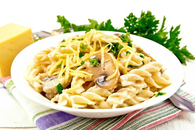 Fusilli-Nudeln mit Pilzen in cremiger Sauce, Petersilie und geriebenem Käse in einer Schüssel auf einem Handtuch auf Holzbretthintergrund