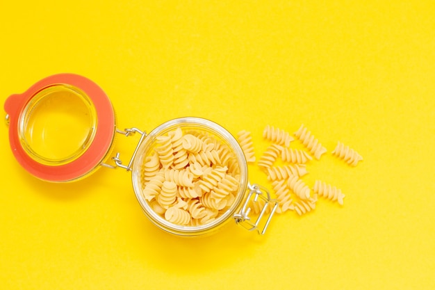 Fusilli pasta macarrones en frasco de vidrio abierto sobre un amarillo