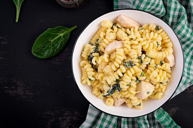 Fusilli-Pasta mit einer cremigen Sauce mit Hühnerfleisch, Parmesan-Käse und Spinat auf einer Schüssel auf dunklem Hintergrund