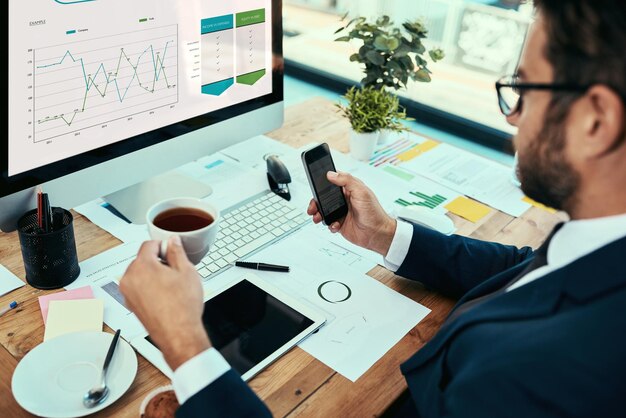 Fusionando toda su tecnología con éxito Foto de un joven empresario bebiendo una taza de té mientras trabajaba en una oficina