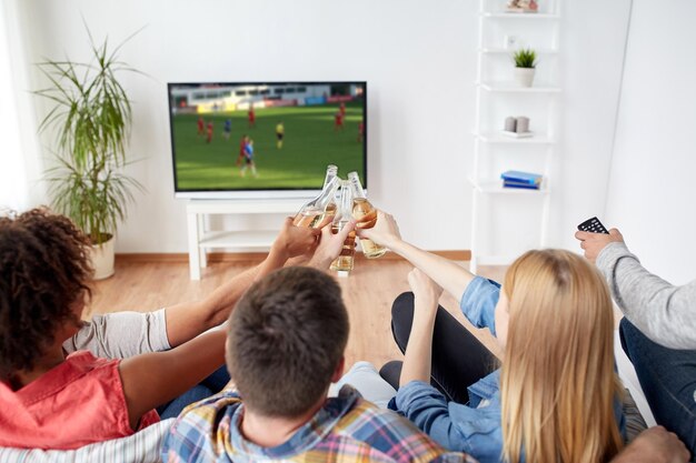 Fußball Freizeit und Menschen Konzept glückliche Freunde klingeln Bierflaschen und beobachten Fußballspiel im Fernsehen zu Hause