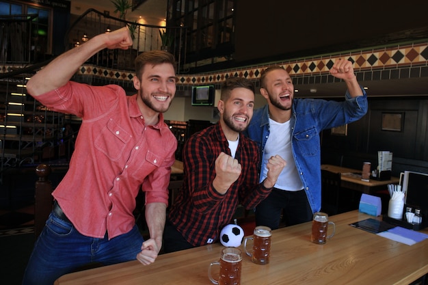 Fußball gucken in der Bar. Fröhliche Freunde, die Bier trinken und für das Lieblingsteam jubeln und den Sieg feiern.