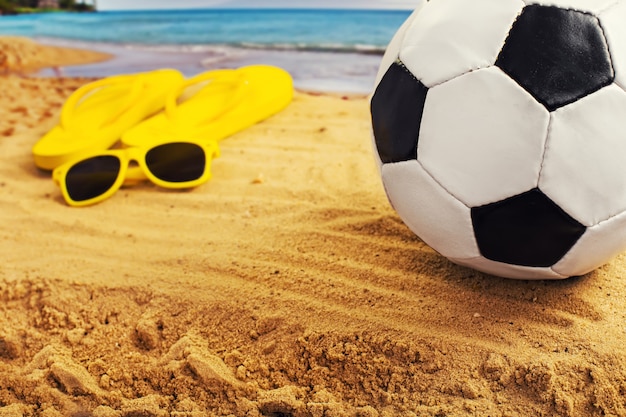 Fußball im Sand mit Sandalen am Strand