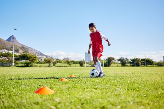 Fußball-Mädchen-Kind-Training und Gras für Fitness-Geschwindigkeit oder Gleichgewicht mit Kontrolle und Geschwindigkeit der Sporttalententwicklung Weibliches Kind schnelles Fußball-Dribbling oder Motivations-Mentalität auf dem Feld in Kapstadt