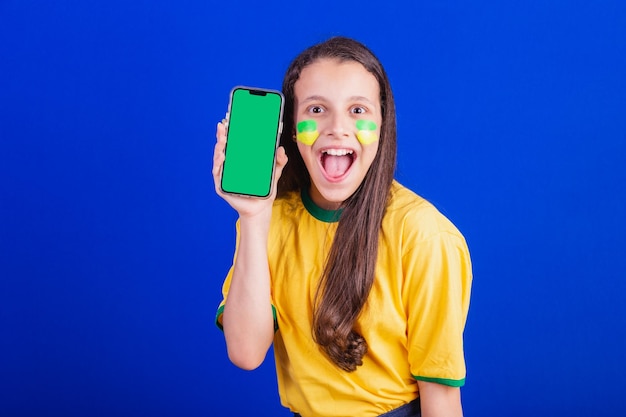 Fußballfan eines jungen Mädchens aus Brasilien, das einen Handybildschirm für die Werbung für Smartphone-Anwendungen hält