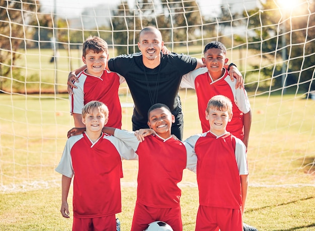 Fußballkinder und Porträt eines Trainers mit seinem Team auf einem Außenplatz nach einem Spiel oder Training Fußballsport- und Kindergruppe, die mit einem Trainer auf einem Spielfeld für Spielübungen oder Übungen steht