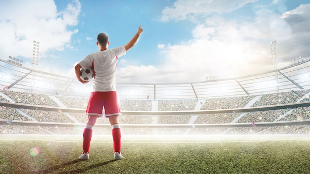 Fußballkonzept. Der Fußballspieler hält einen Fußball im Profistadion und spricht mit den Fans.