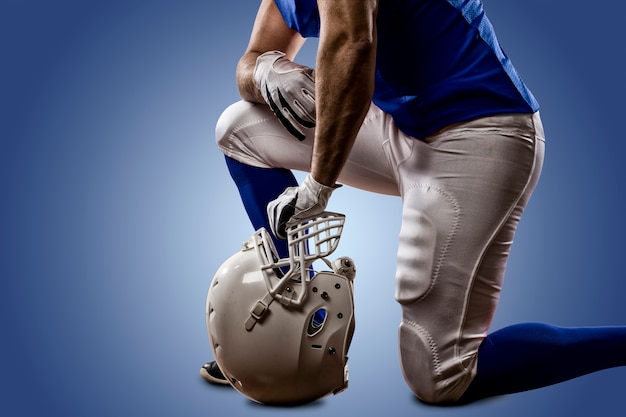 Fußballspieler mit einer blauen Uniform auf den Knien an einer blauen Wand