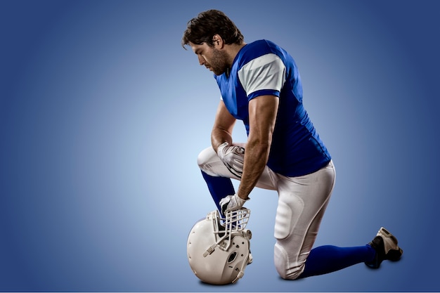 Fußballspieler mit einer blauen Uniform auf den Knien an einer blauen Wand