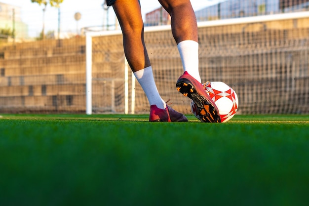 Fußballspielerfüße, die mit dem Ball vor dem Feld laufen Fußballspieler auf dem Feld, der mit dem Ball läuft