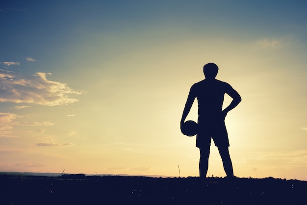 Fußballspielermann, der hintere ansicht im schattenbild lokalisiert auf sonnenunterganghintergrund steht