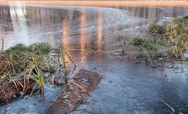 Fußgängerbrücke im Eisfluss im frühen Winter Es gibt etwas Schilf auf einem Backgroung des blauen Eises mit Luftblasen Winterlandschaftsszene