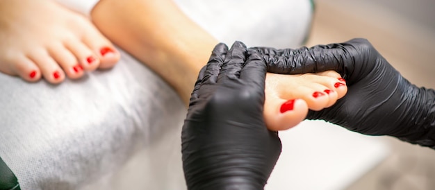 Fußmassage mit Feuchtigkeits- und Peelingcreme durch Fußpflegerhände mit schwarzen Handschuhen, Nahaufnahme.