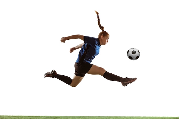 Foto futebol feminino jovem ou jogador de futebol com cabelo comprido, chutando a bola para o gol em vôo, pulando alto no fundo branco do estúdio. conceito de estilo de vida saudável, esporte profissional, movimento, movimento.