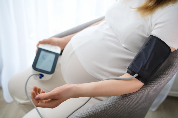 La futura madre controla la presión arterial con un instrumento de medición La mujer se sienta cómodamente en una silla