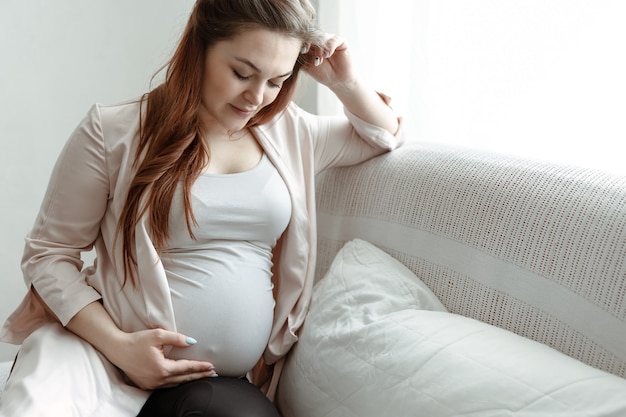 La futura madre con una gran barriga está sentada en el sofá de su casa.