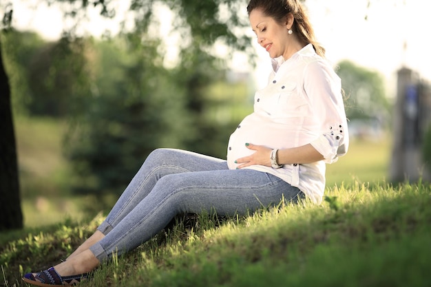 La futura madre se sienta en el césped de un parque en un día soleado