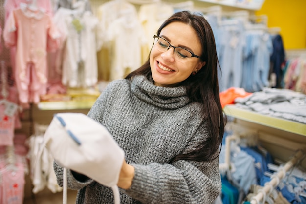 La futura madre sonriente elige un gorro de bebé en la tienda para recién nacidos.