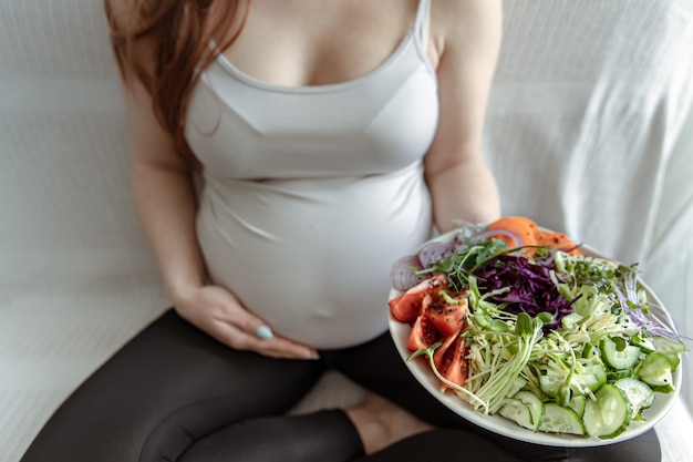 Foto la futura madre en los últimos meses de embarazo sostiene un plato de ensalada de verduras.