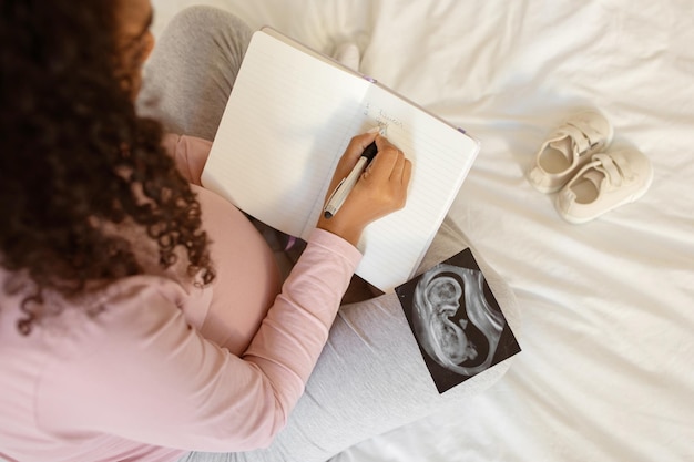 Futura mãe escrevendo em diário ao lado de ultrassom de bebê e sapatos pequenos