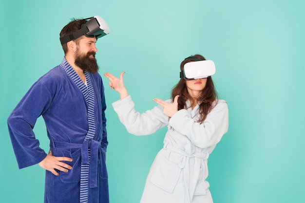 El futuro está más cerca de lo que piensas. El hombre y la mujer exploran la realidad virtual en casa. Tecnología VR y futuro. Comunicación VR. Impresiones emocionantes. Pareja en albornoces usa gafas de realidad virtual. Juegos y entretenimiento.