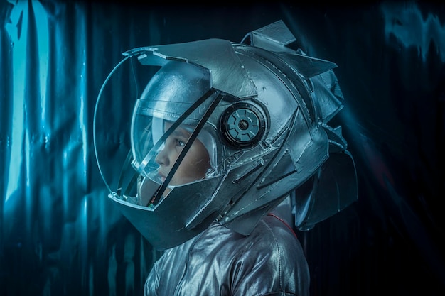 Futuro, niño jugando a ser astronauta con casco espacial y traje de metal sobre fondo plateado