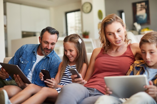 El futuro del tiempo en familia es ahora Fotografía de una joven familia feliz usando dispositivos inalámbricos en el sofá de casa