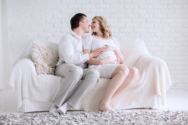 Futuros padres jóvenes sentados en el sofá de la sala de estar. el concepto de felicidad familiar