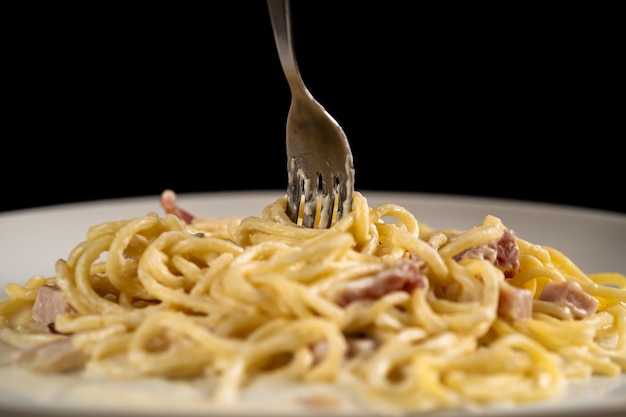 Gabel dreht Carbonara-Spaghetti auf weißem Teller auf schwarzem Hintergrund