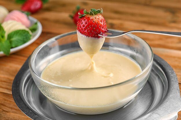 Gabel mit frischer Erdbeere, eingetaucht in weiße Schokoladenfondue-Nahaufnahme