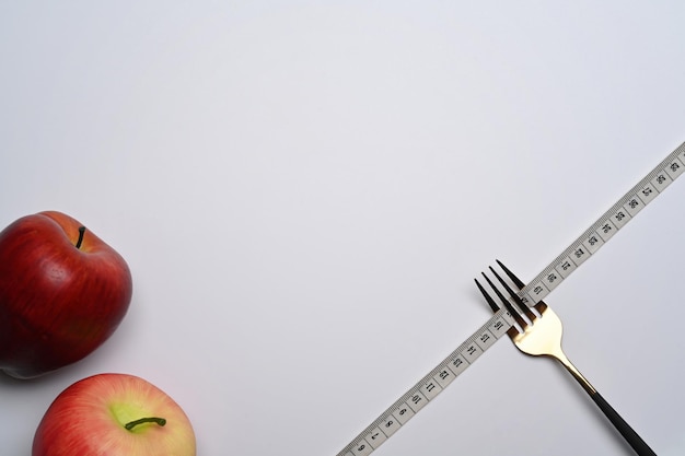 Gabel mit Maßband und Äpfel auf weißem Hintergrund Gewichtsverlust und gesunde Ernährung Konzept
