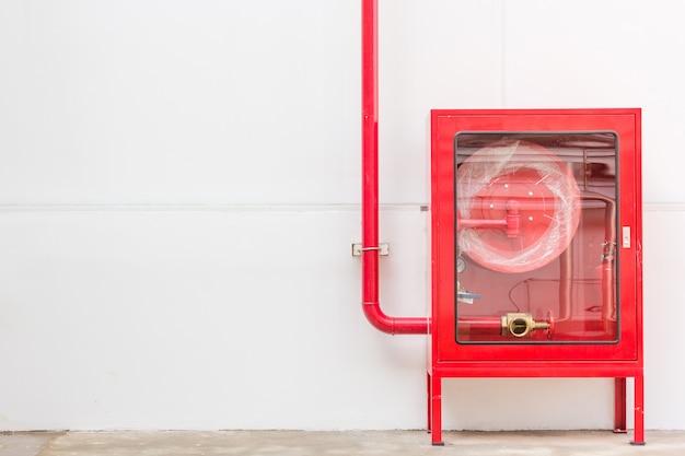 Gabinete y extintor de manguera roja contra incendios en pared blanca en la nueva fábrica de edificios