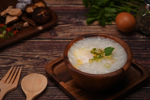 Gachas de arroz con jengibre en rodajas de huevo cocido y cebollín en un tazón sobre una mesa de madera Desayuno chino tradicional