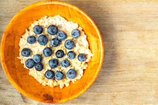 Gachas de avena y arándanos en tazón de bambú naranja sobre mesa de madera