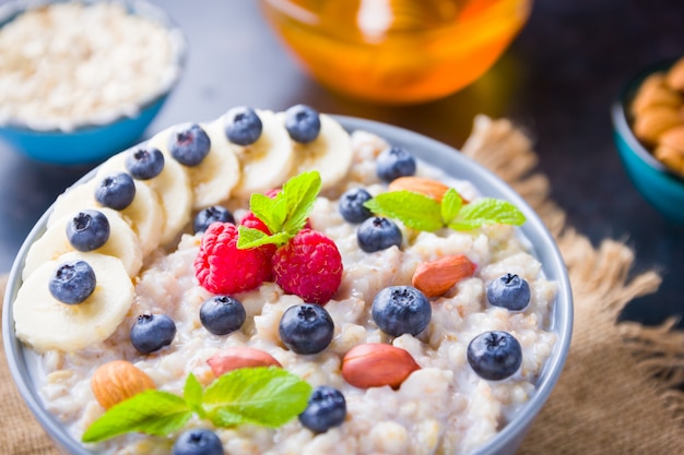 Gachas de avena con bayas, frutas y miel sobre fondo oscuro