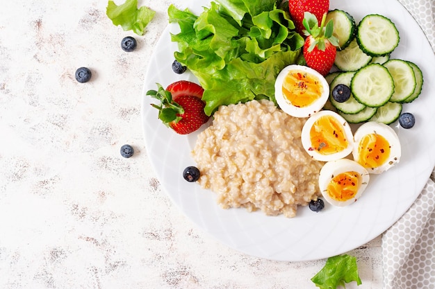 Gachas de avena para el desayuno con huevos cocidos, pepino y fresa Comida sana y equilibrada Vista superior endecha plana