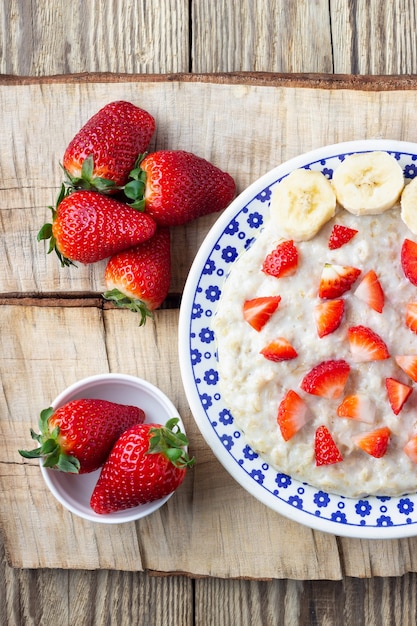 Foto gachas de avena con fresas y plátano sobre un fondo de madera. desayuno saludable con bayas orgánicas frescas. vista superior.