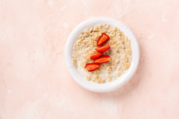 Gachas de avena con fresas en un plato blanco sobre una servilleta de lino sobre fondo rosa. Concepto de comida sana de desayuno. Vista superior