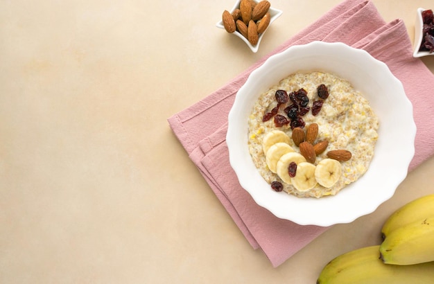 Gachas de avena con leche con plátano, arándanos secos y almendras sobre fondo beige, espacio para texto