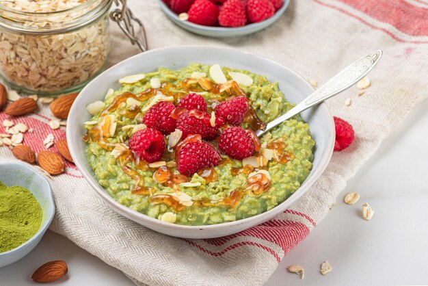 Gachas de avena matcha en un tazón con nueces de frambuesas maduras frescas y salsa de caramelo para un desayuno saludable