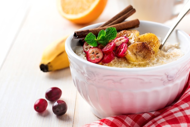 Gachas de avena con plátanos horneados, canela, naranja y arándanos en un cuenco de cerámica sobre una superficie clara. Enfoque selectivo.