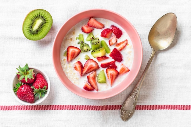 Gachas de avena con rodajas de kiwi, fresas, almendras en una cuchara de tazón rosa sobre un mantel blanco