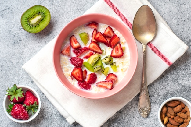 Gachas de avena con rodajas de kiwi fresas almendras en cuenco rosa cuchara servilleta con rayas rojas ...