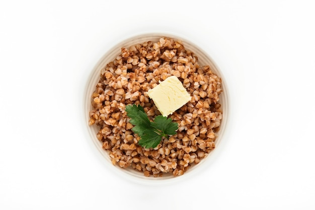 Gachas de avena de trigo sarraceno en un tazón con hojas de perejil y mantequilla aislado en blanco. Grano antiguo sin gluten para una dieta saludable