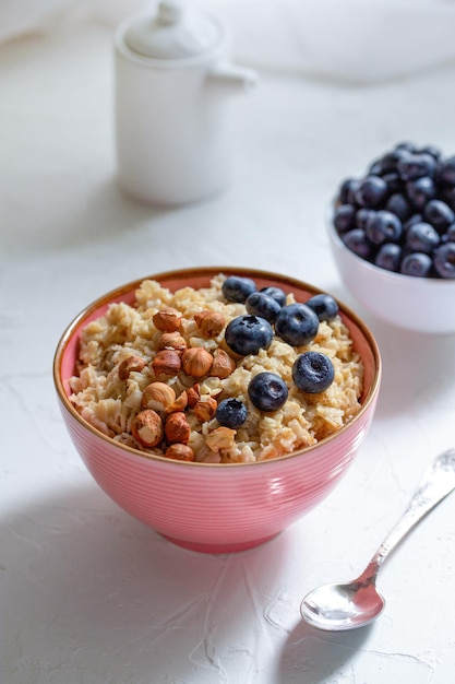 Gachas hercúleas con granola de avellanas y arándanos en una placa rosa o mesa blanca