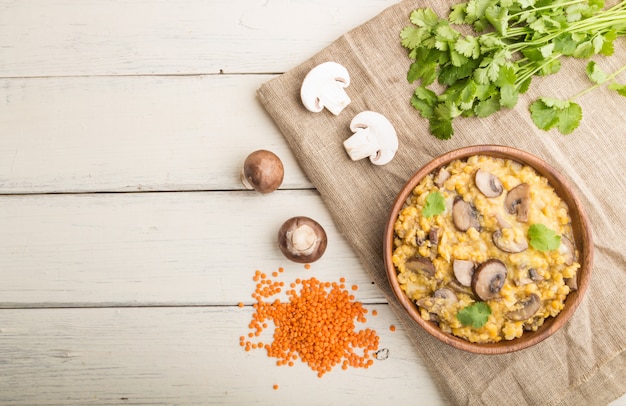 Gachas de lentejas con champiñones y cilantro en un recipiente de madera sobre un fondo blanco de madera. Vista superior, copia espacio.