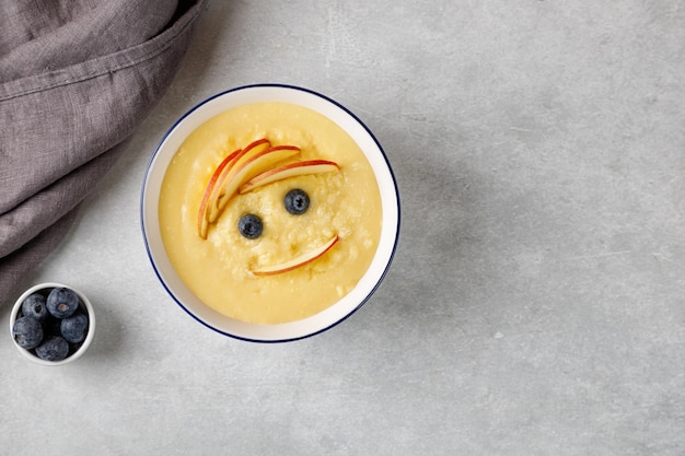 Gachas de maíz para niños con frutas, arándanos y manzana sobre fondo gris