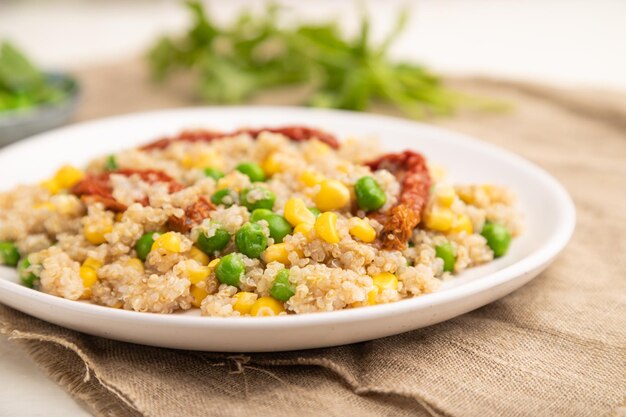 Gachas de quinoa con maíz de guisantes verdes y tomates secos en placa de cerámica sobre un fondo de madera blanca Enfoque selectivo de vista lateral