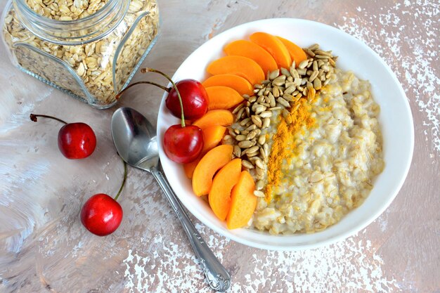 Gachas saludables con rodajas de melocotón fresco, semillas de girasol, cúrcuma decorada con cerezas.